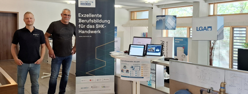 Zwei Männer zeigen an einem Infostand die Prototypen aus dem Projekt learn.SHK