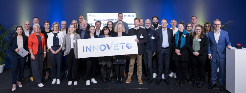 Aur einer Bühne sind ca. 30 Personen zu einem Gruppenbild versammelt, um den Start des Innovationswettbewerbs für exzellente berufliche Bildung, InnoVET PLUS, zu zelebrieren.